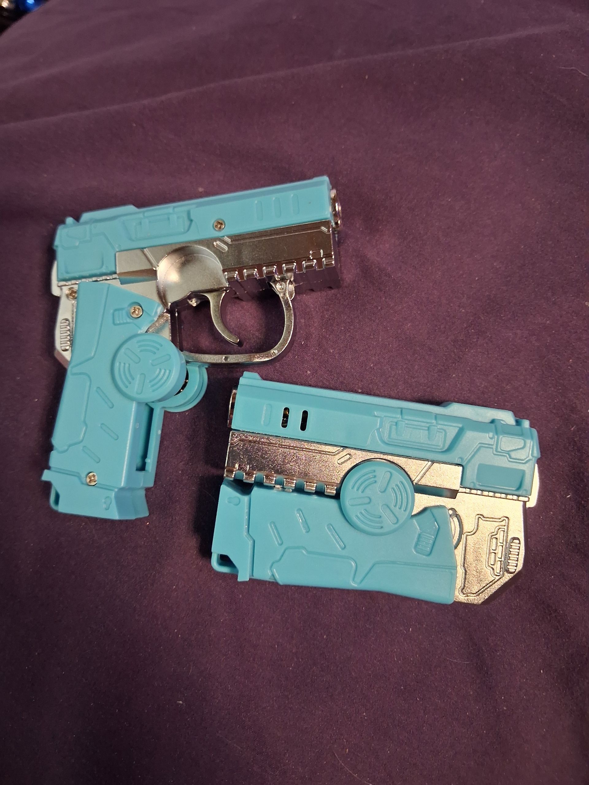 Two blue toy pistols with glitter details on a purple fabric background