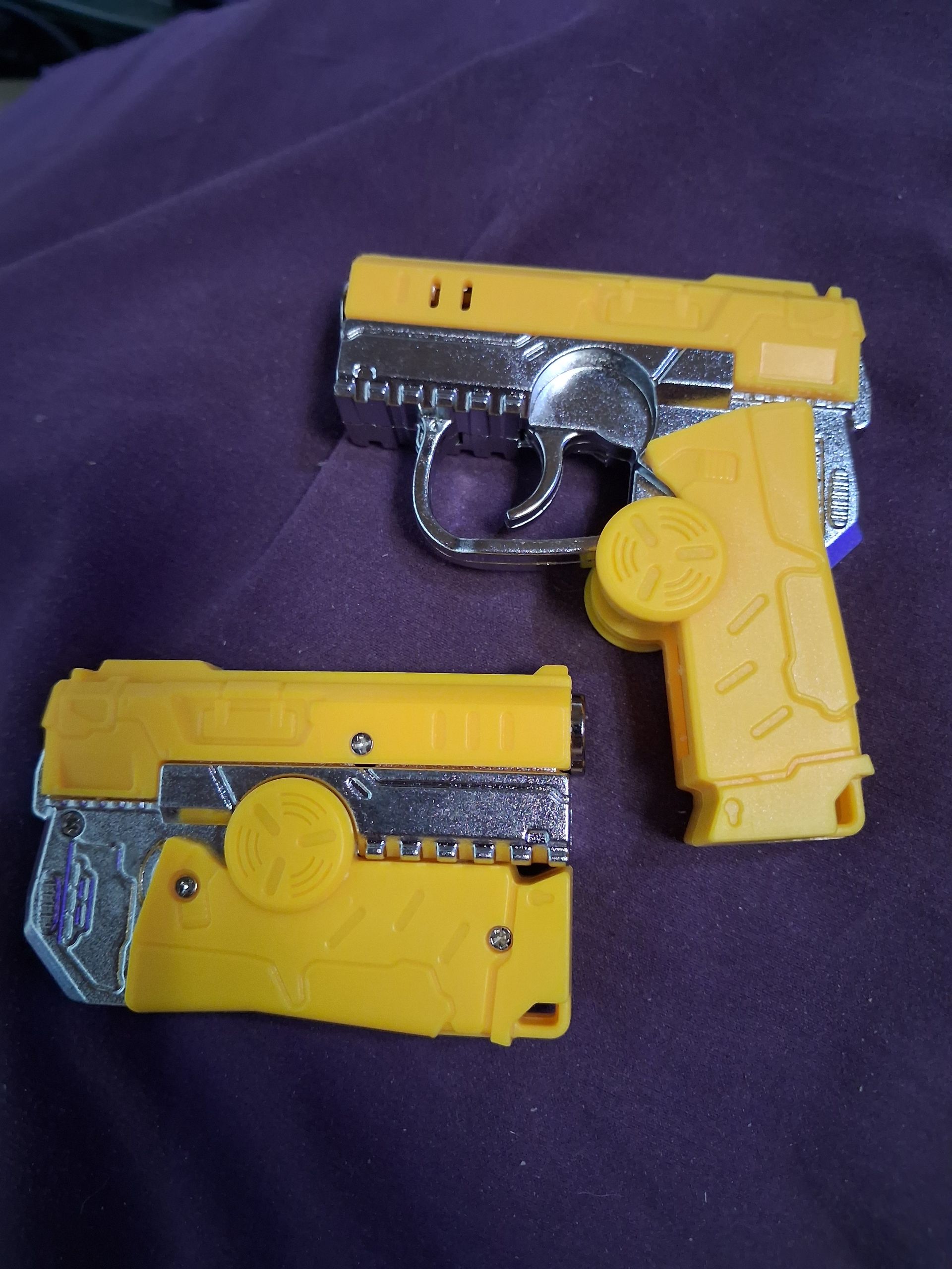 Two yellow toy pistols with black and silver details on a purple cloth background