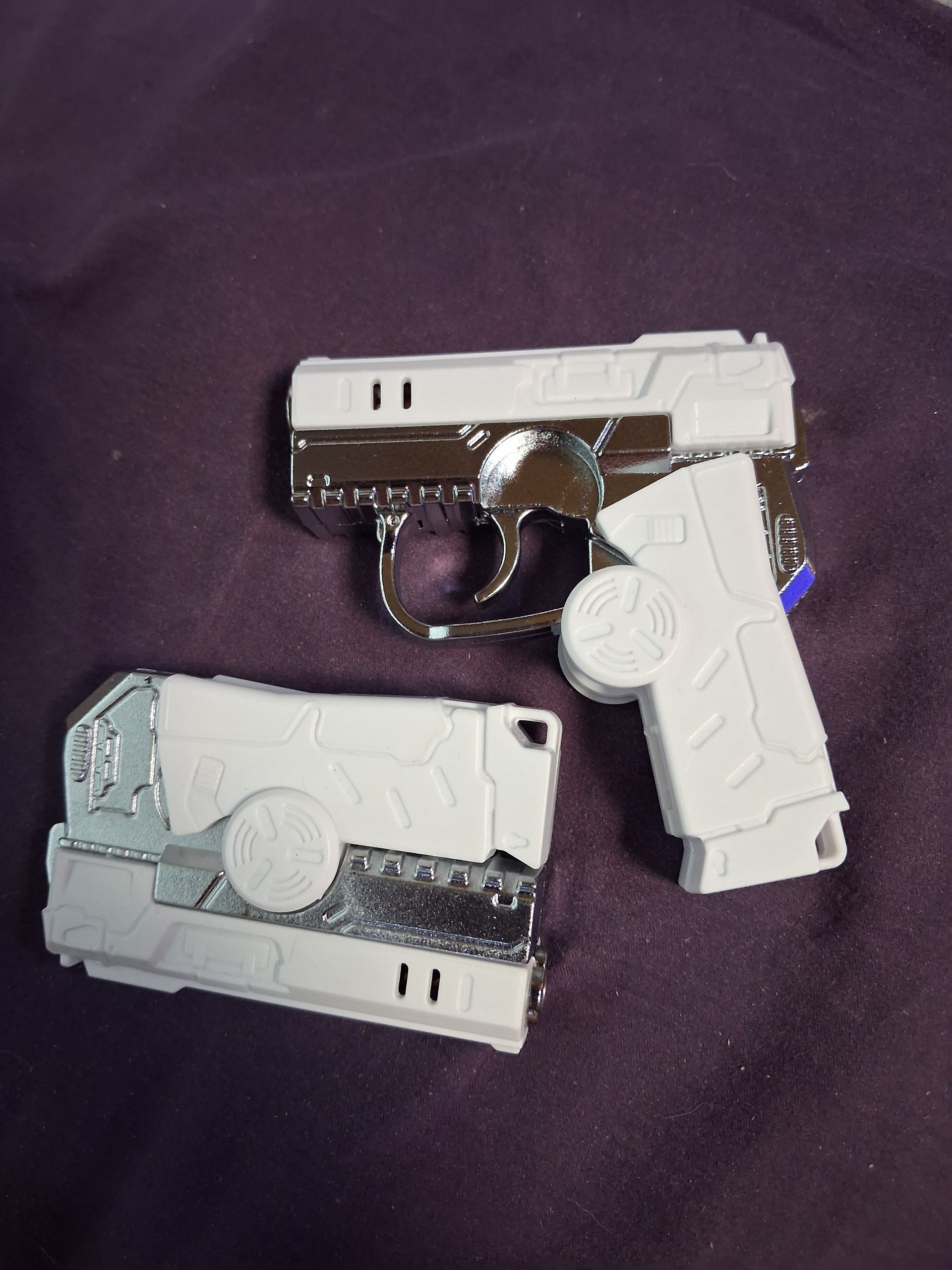 Two toy handguns, one white and one gray, on dark purple fabric.
