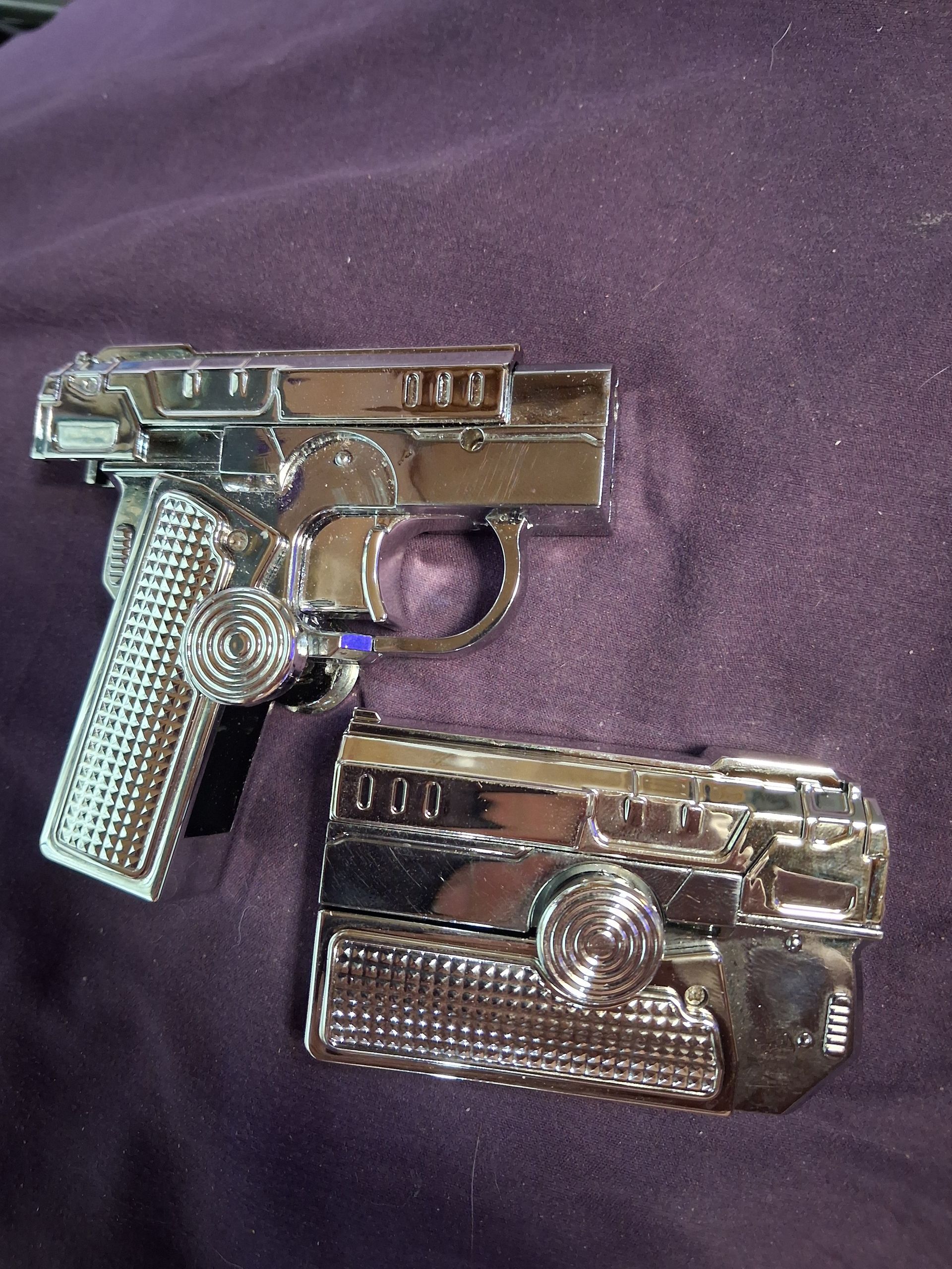 Two toy pistols, one metallic silver and one chrome, lying on purple fabric.