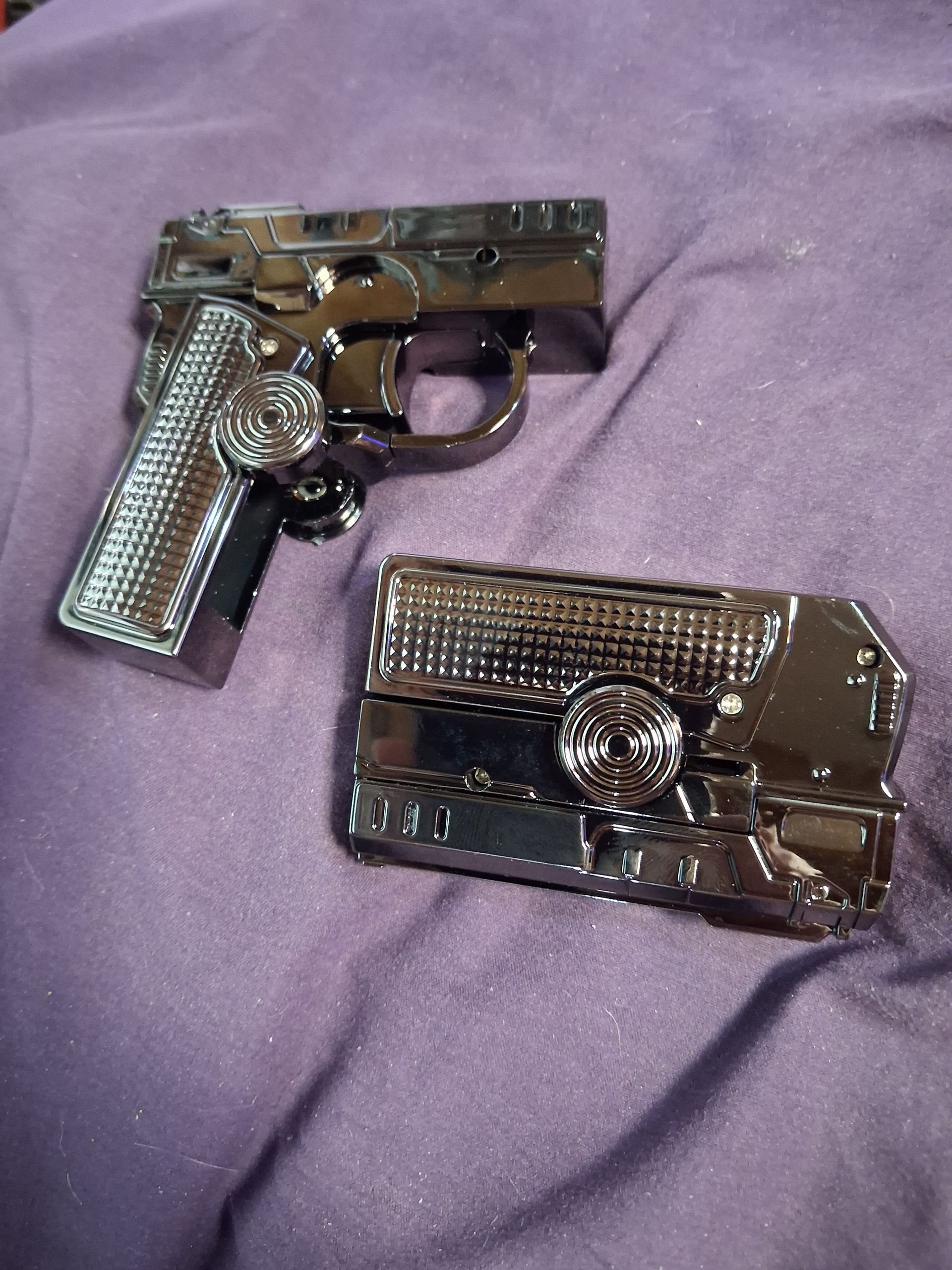 Two toy guns: a silver pistol and a small revolver on a purple fabric background