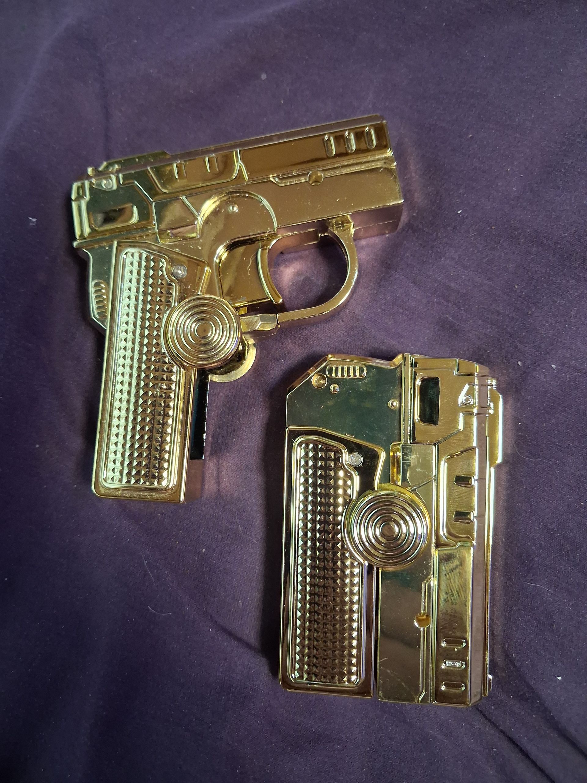 Two gold-colored miniature pistol-shaped objects on purple fabric, one larger and one smaller, side by side