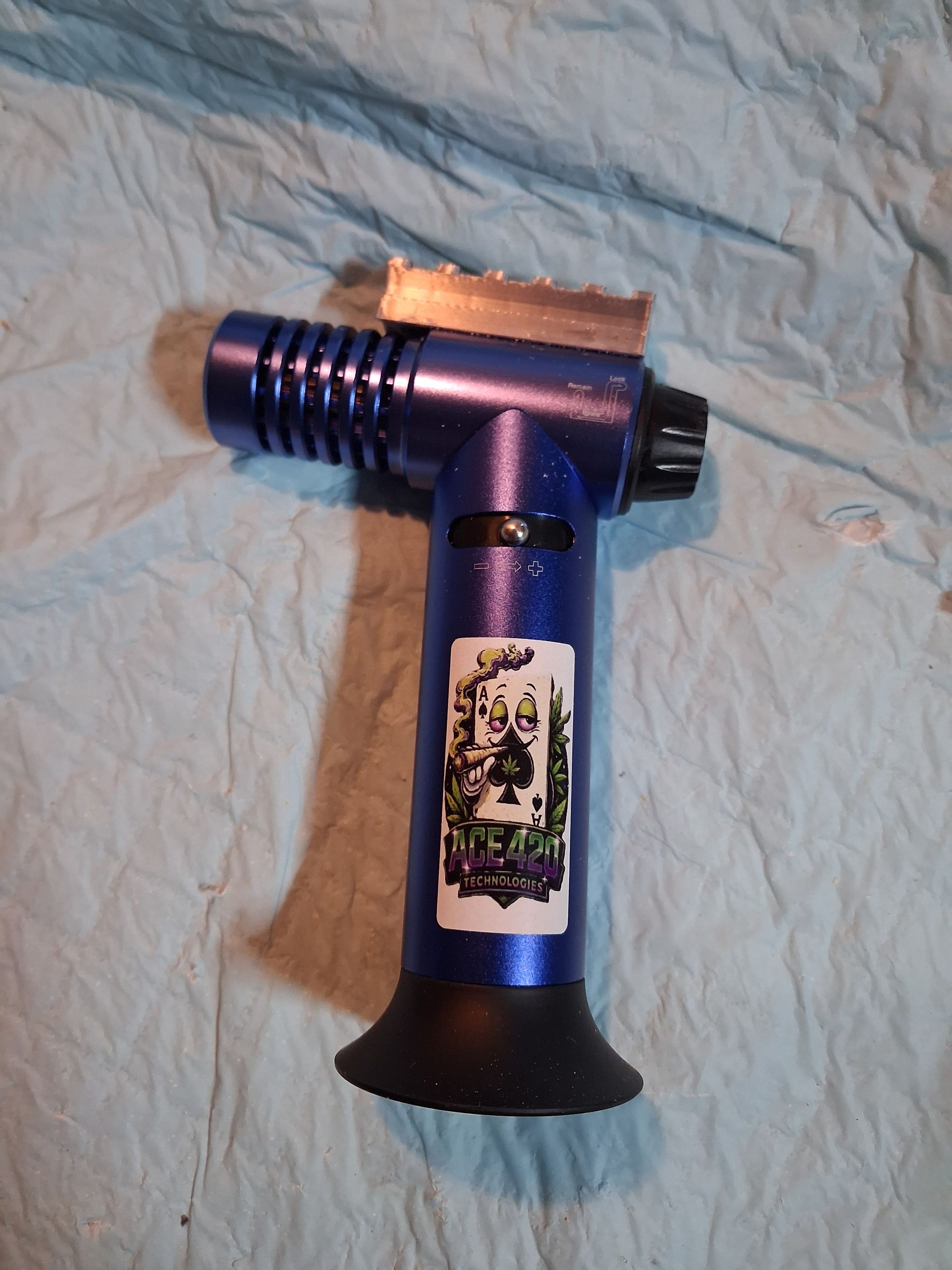 Purple handheld butane torch lighter with black base and silver nozzle on a blue cloth background