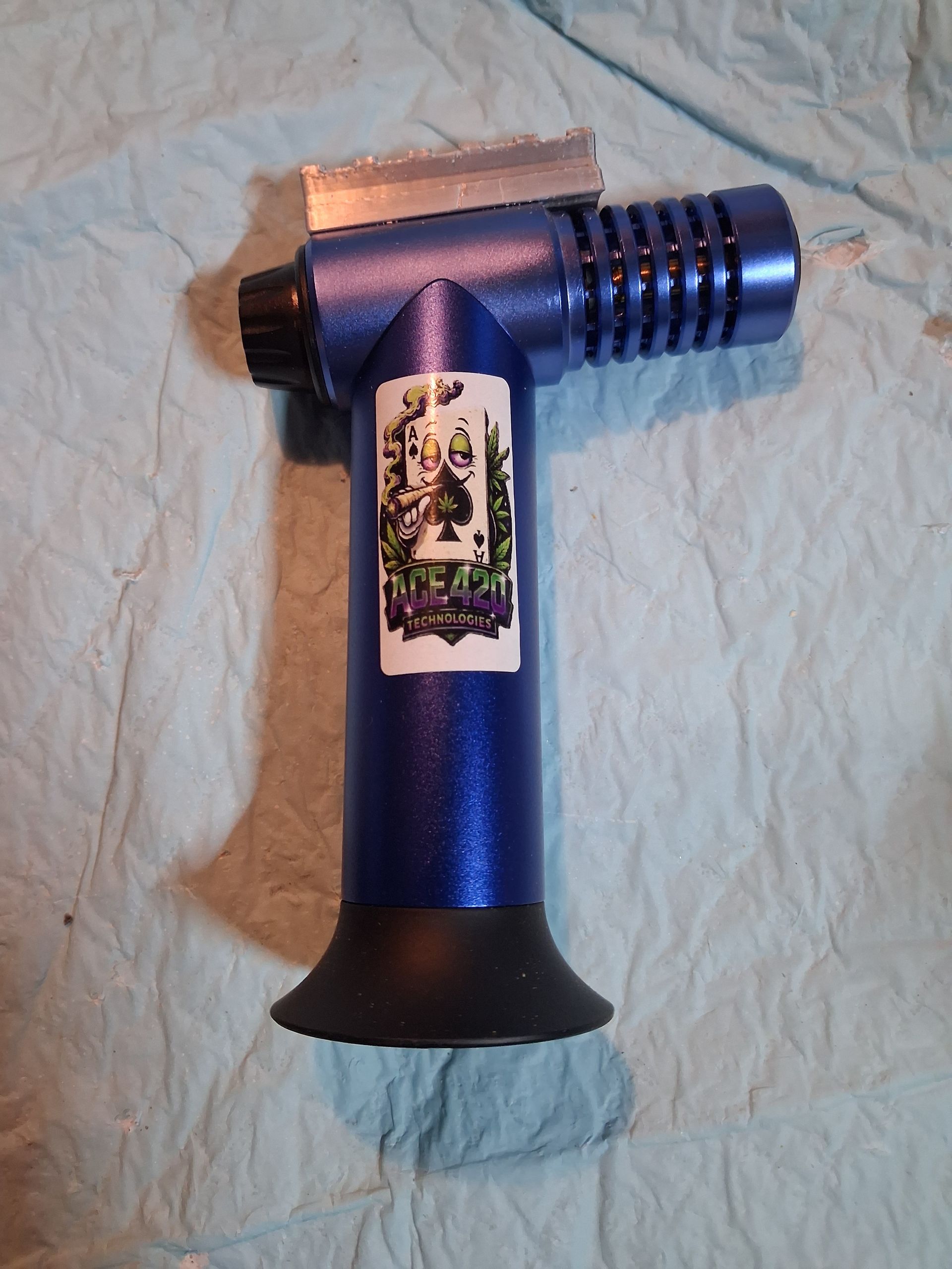 Blue propane torch with fluted nozzle and base, lying on a wrinkled light-colored cloth.