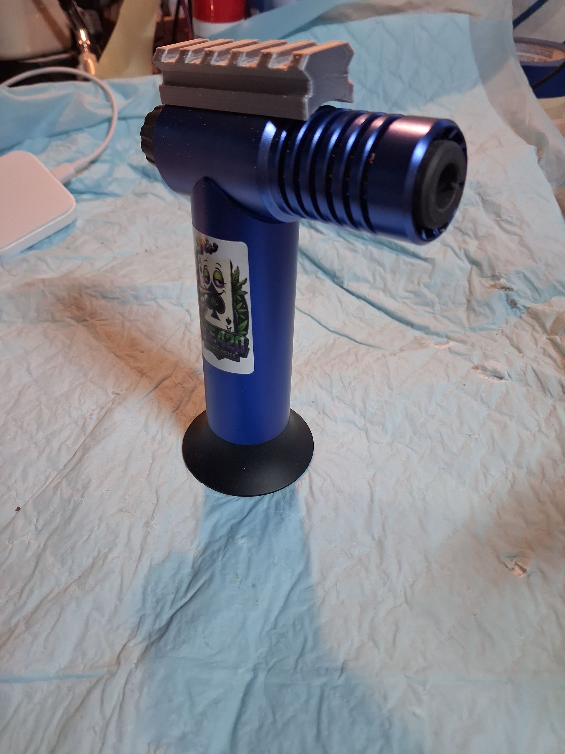 Blue handheld butane torch with fluted nozzle and base on a light blue cloth background