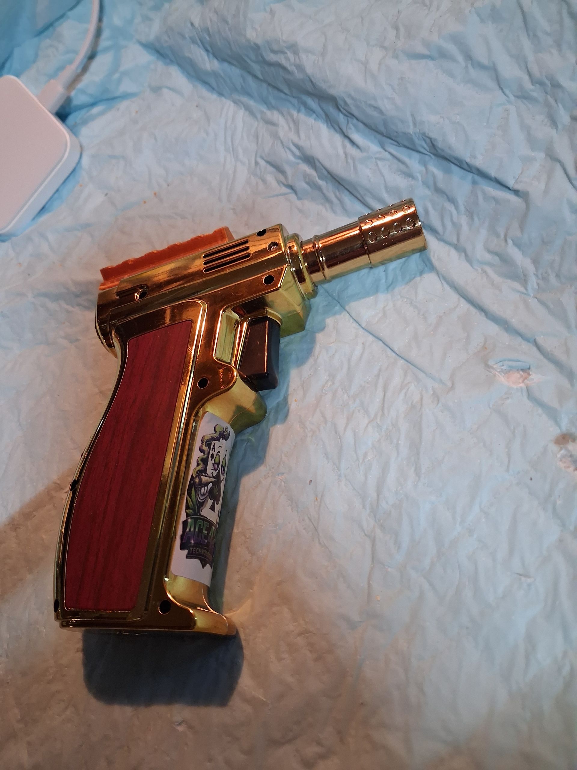 Gold-colored butane torch with a red grip on a blue fabric surface