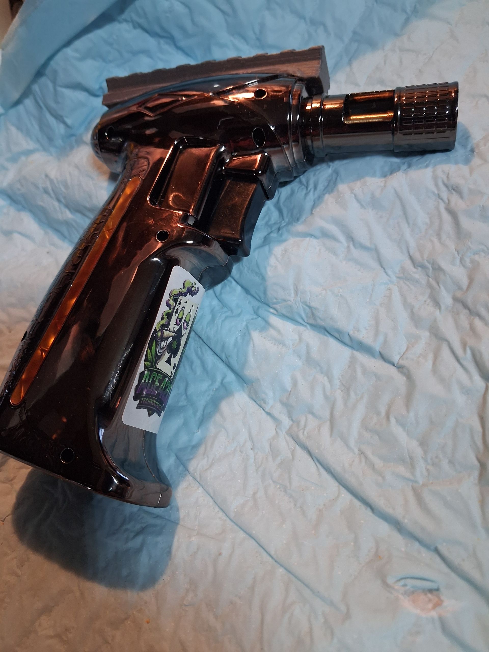 Black handheld butane torch with a rail lying on blue cloth.