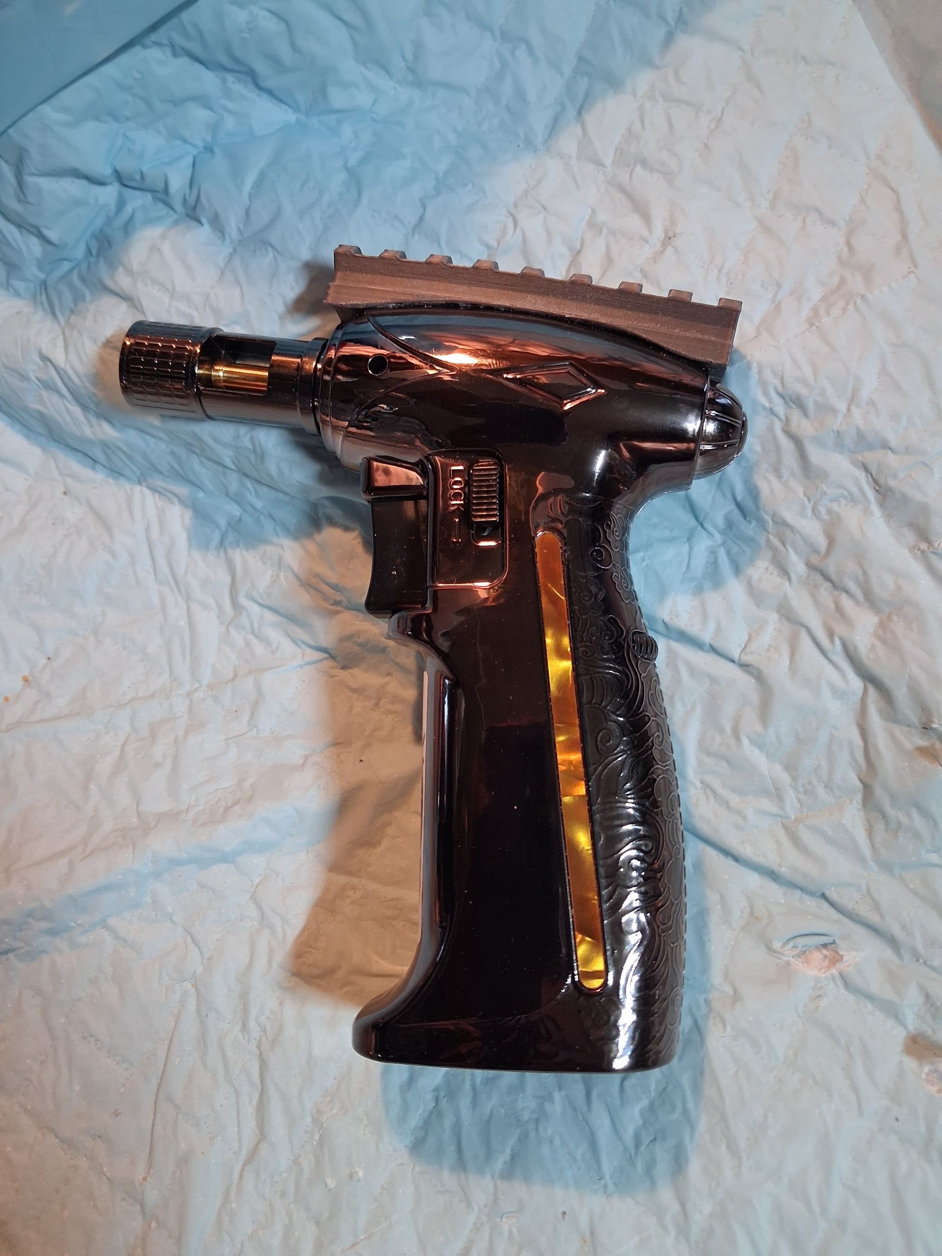 Black handheld butane torch on a light blue quilted surface