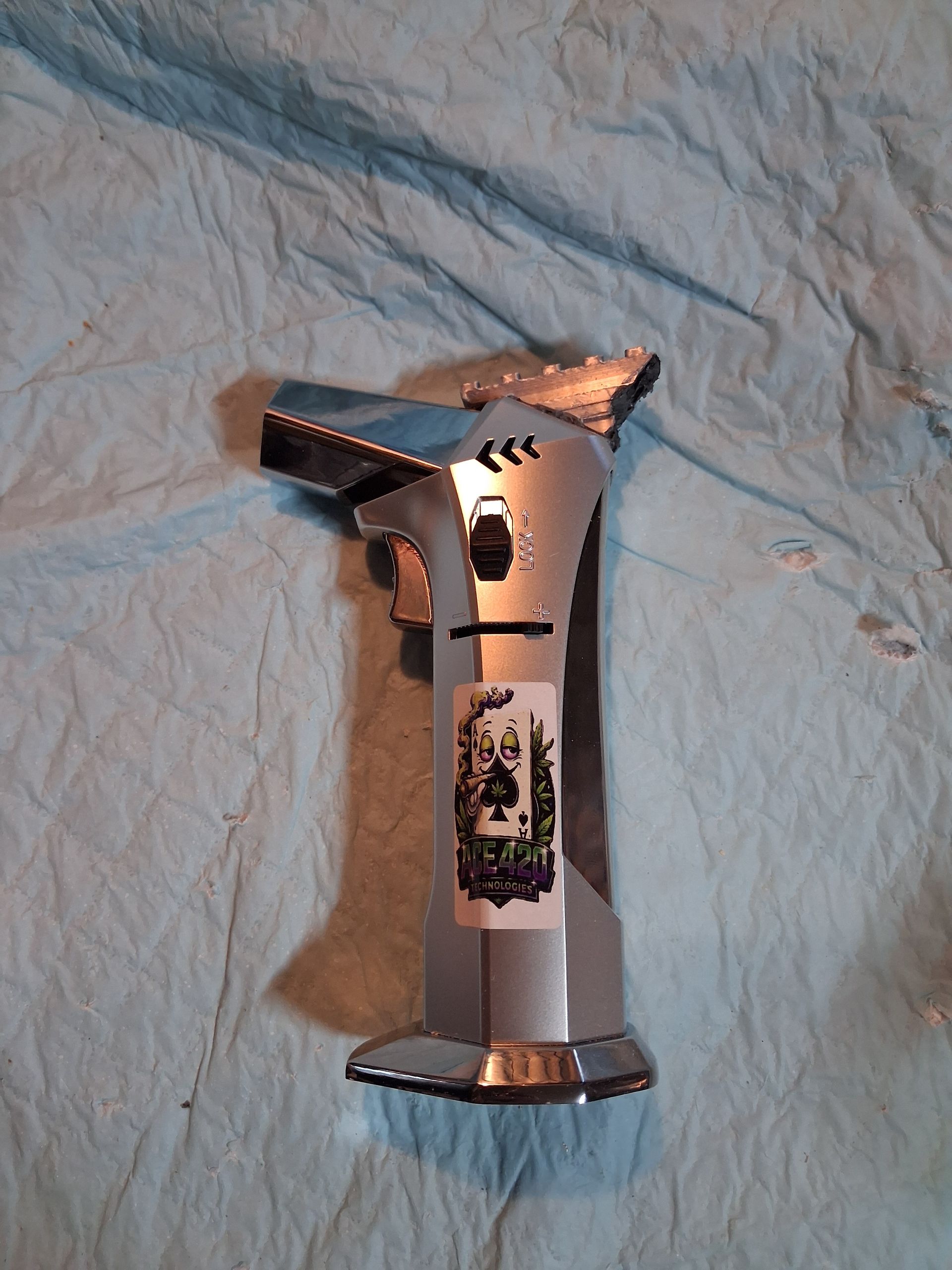 Silver butane torch lighter with Logo sticker on a wrinkled light blue cloth background