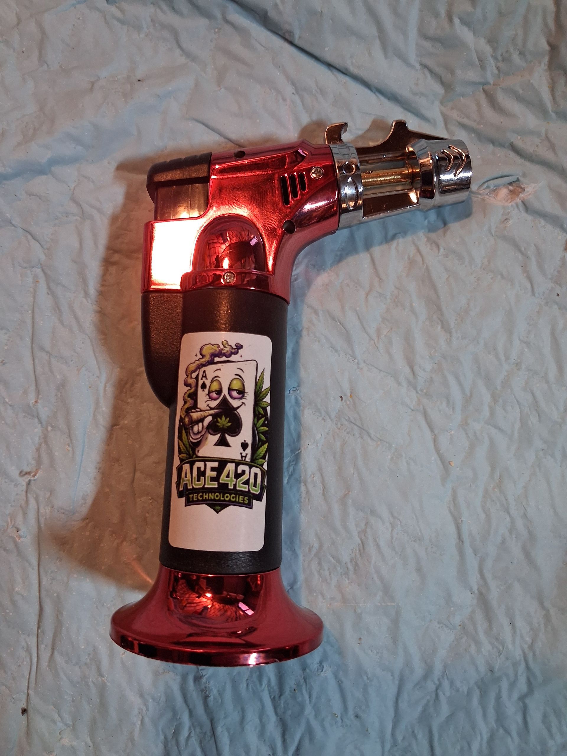 Red metallic butane torch lighter with a bottle opener on a light fabric surface