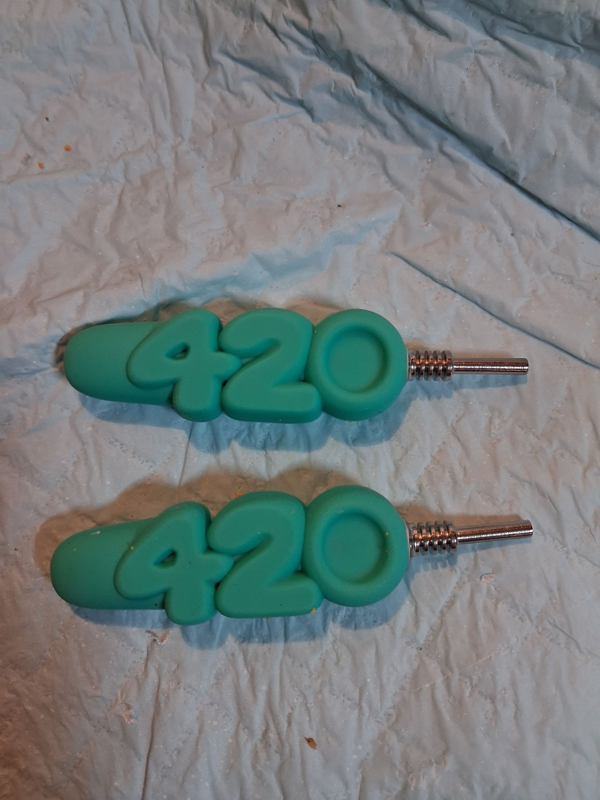 Two turquoise “420” keychains with silver chains on a light wrinkled fabric background