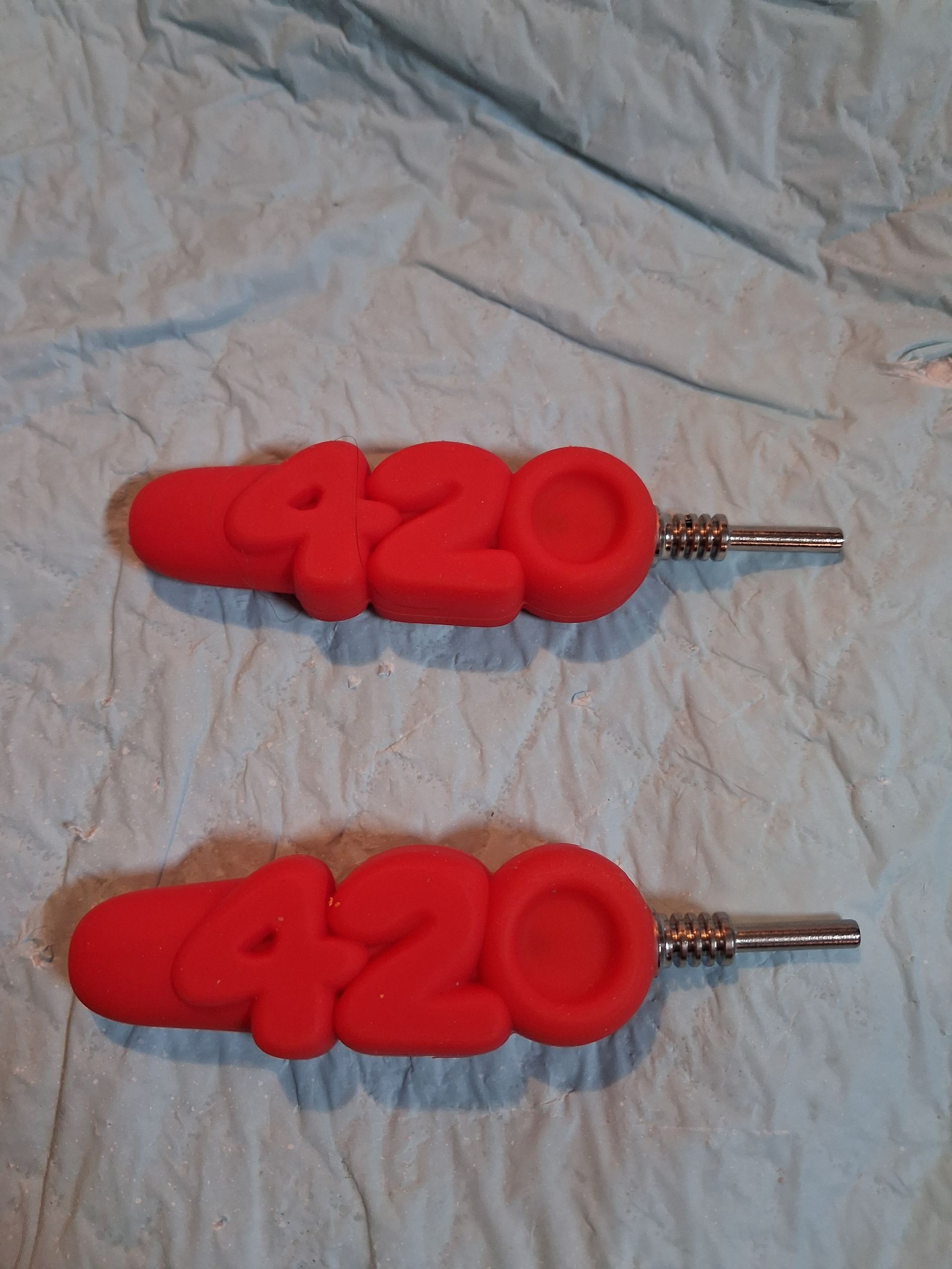 Two red 420 keychain plugs on a light fabric background