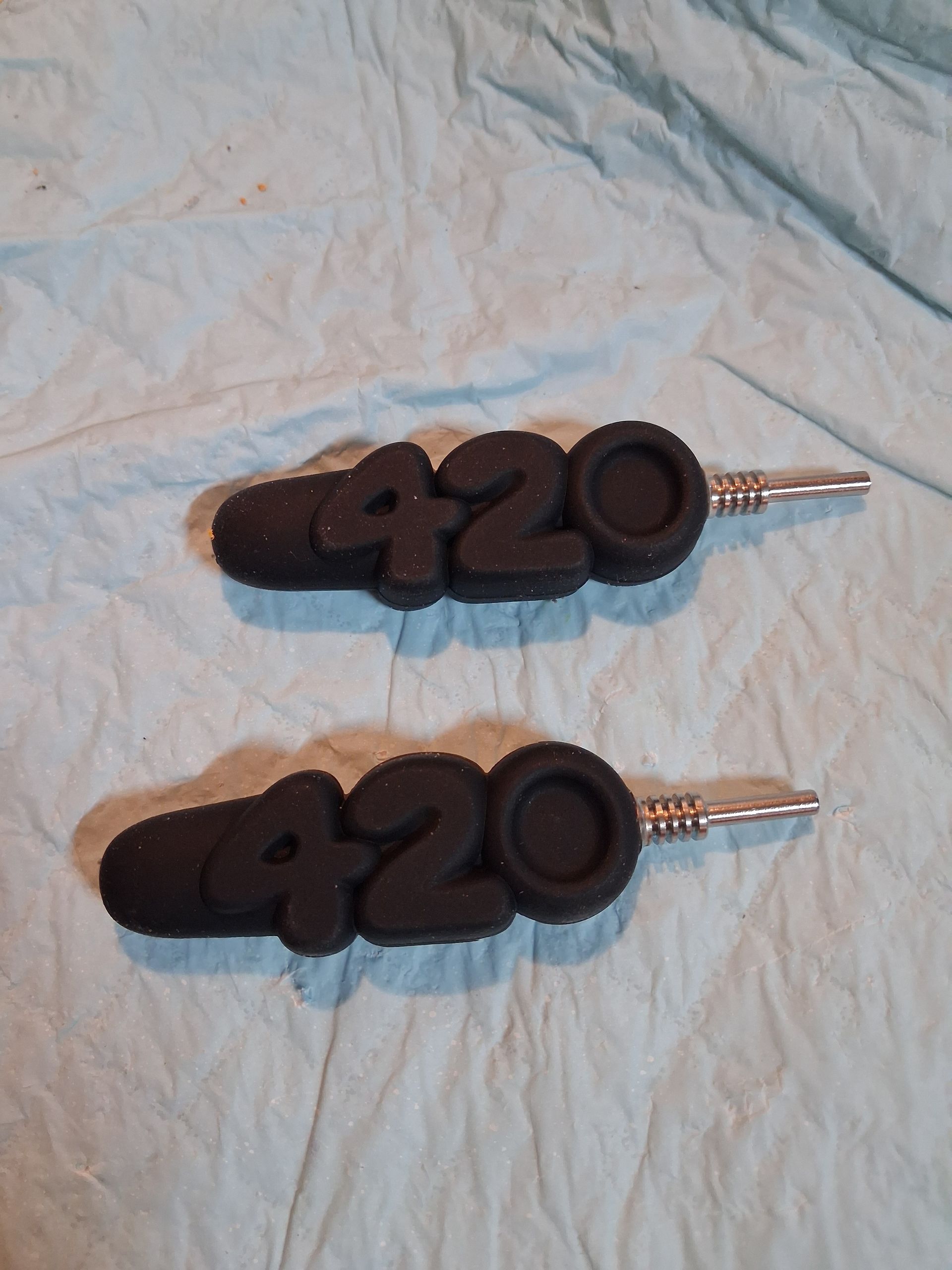 Two black 420-shaped keychains on a wrinkled light blue cloth background