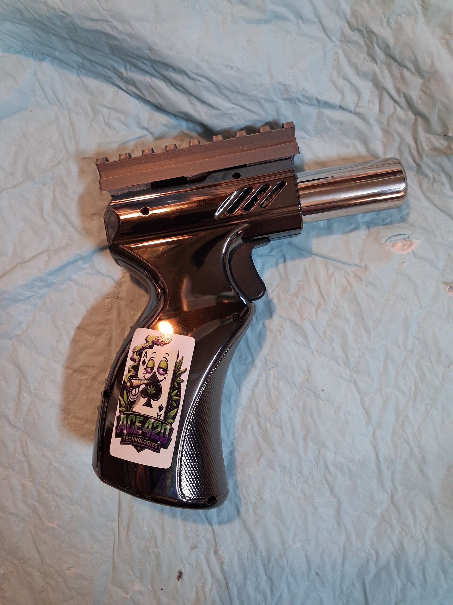 Black gun shaped torch on a light blue blanket, with a shiny silver barrel and a sticker on the grip