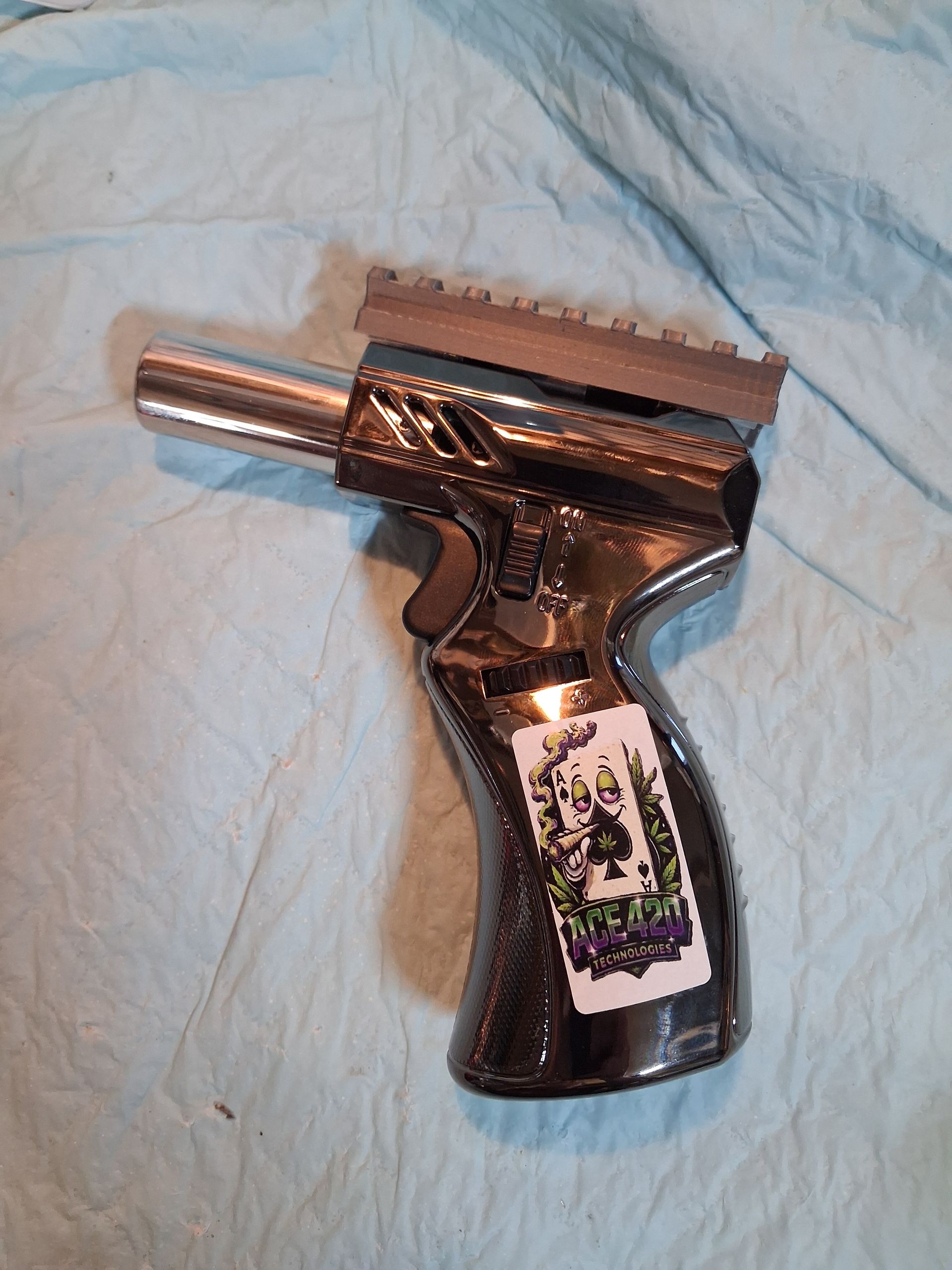 Handheld metal object with a silver nozzle and black handle on a light blue cloth background