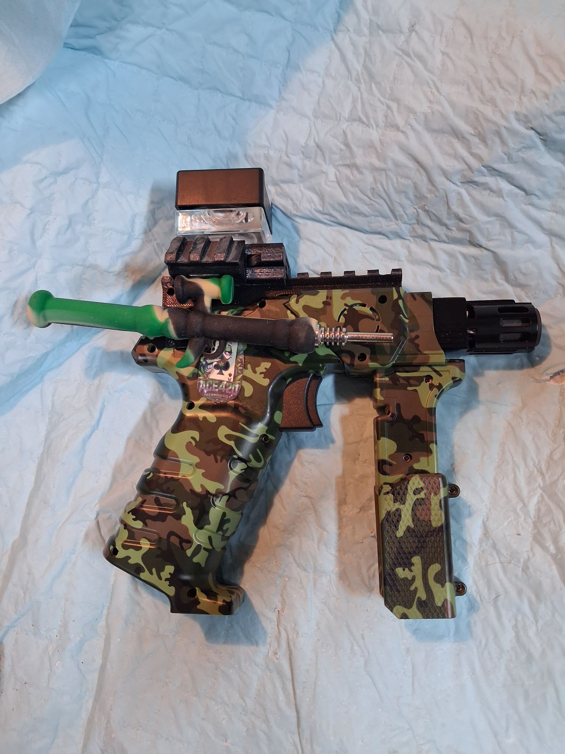 Camouflage toy gun with green barrel tip and magazine on a light blue quilted blanket