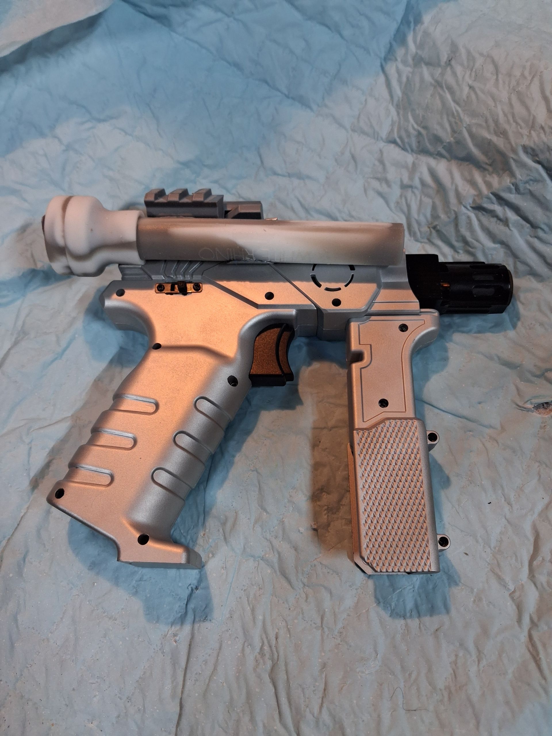 Toy sci-fi handgun on blue cloth, with silver body, tan grip, and black slide.