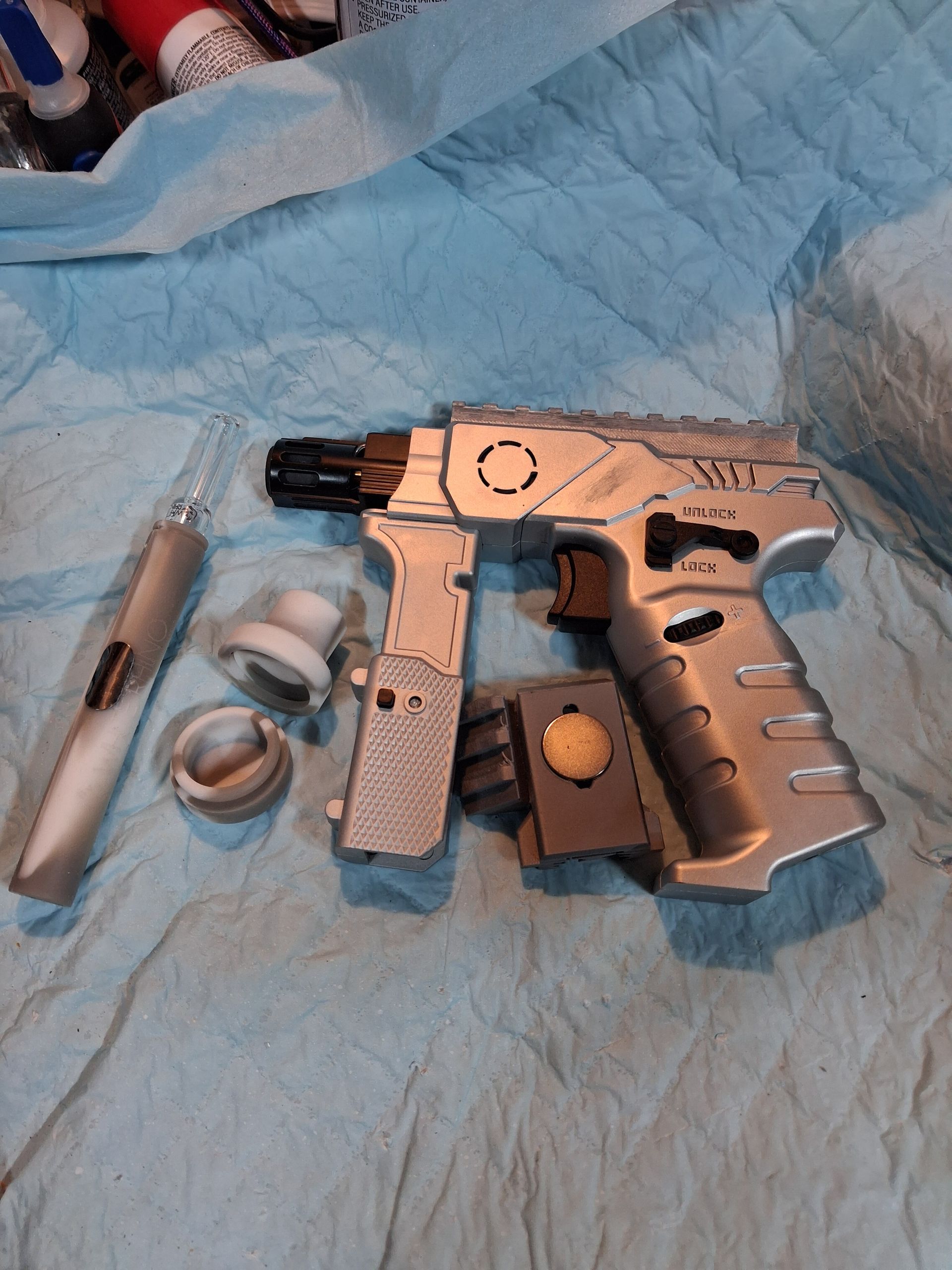 Silver toy pistol with orange tip, lying on blue fabric beside small loose parts and tools