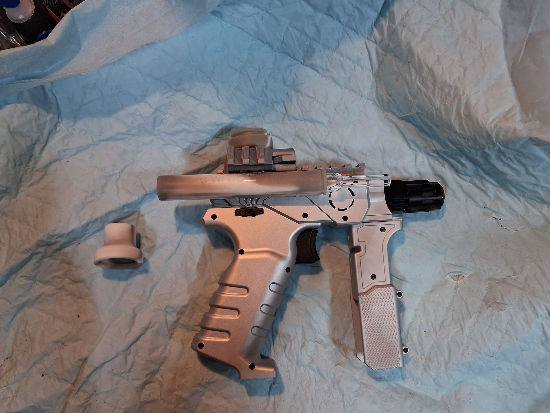White-and-black handgun with accessories on blue crumpled fabric backdrop.