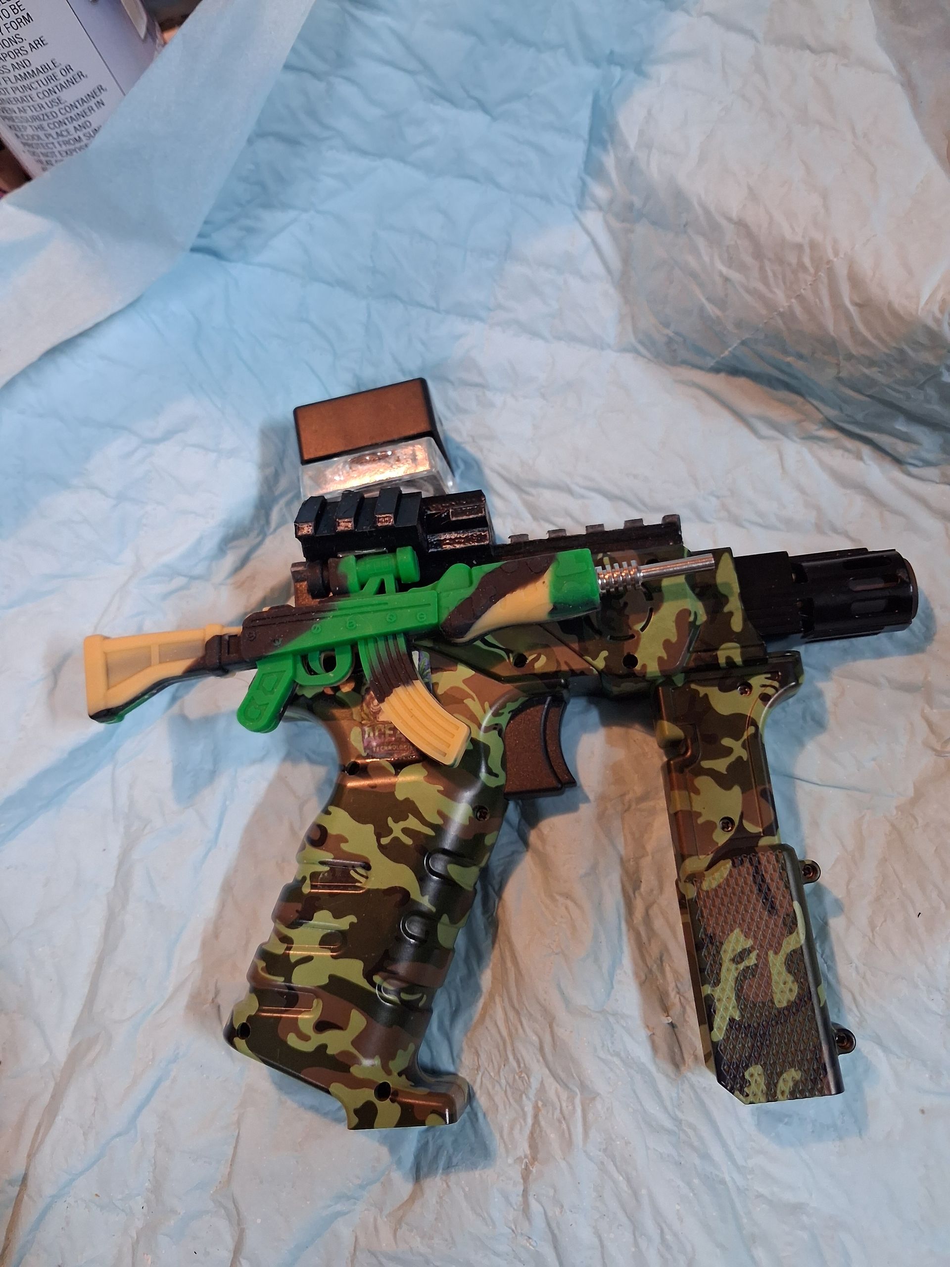 Toy rifle with camouflage parts and green accents lying on a light blue bedspread