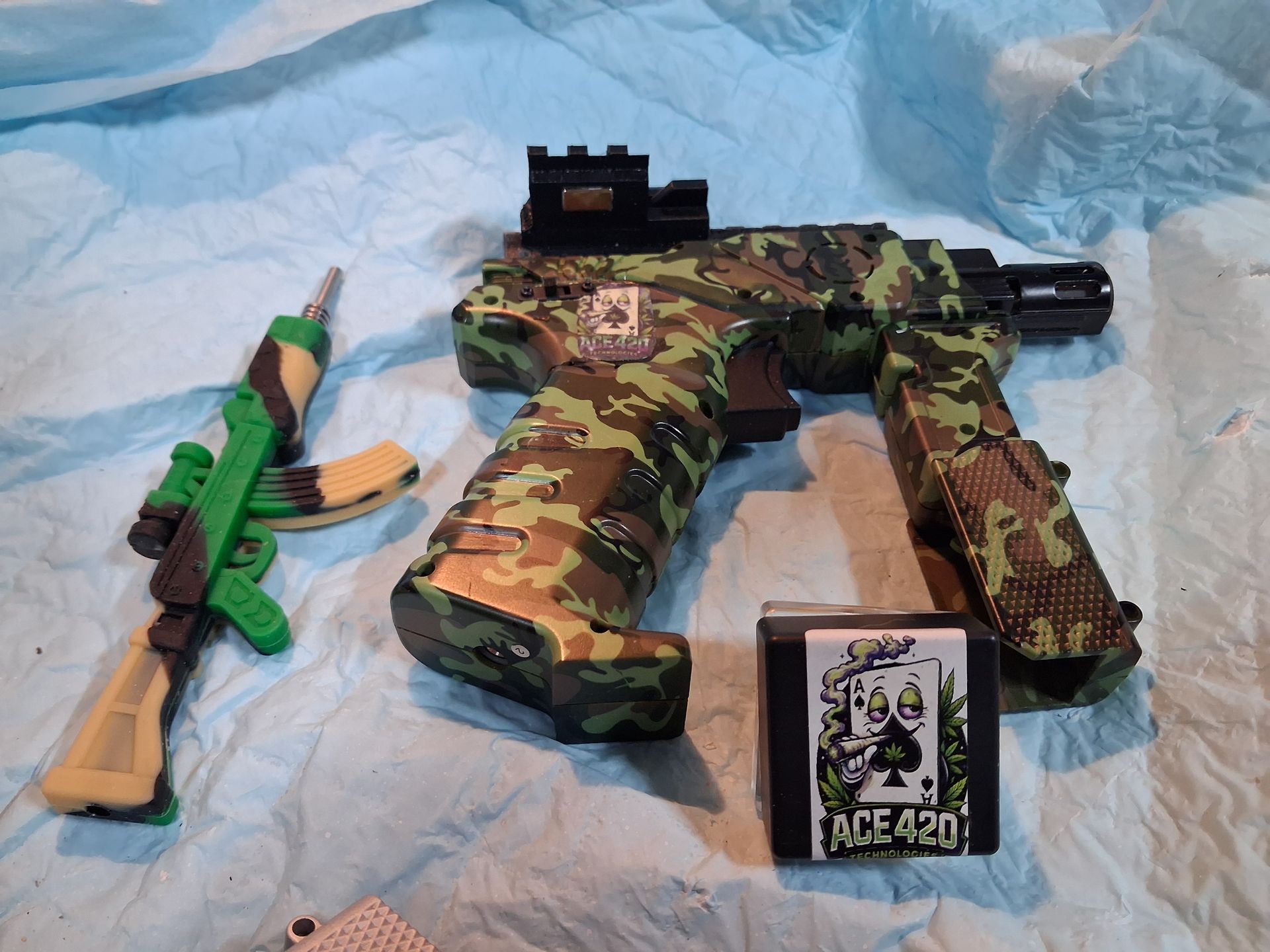 Camouflage toy rifle with green toy gun and trading card on a light blue cloth background