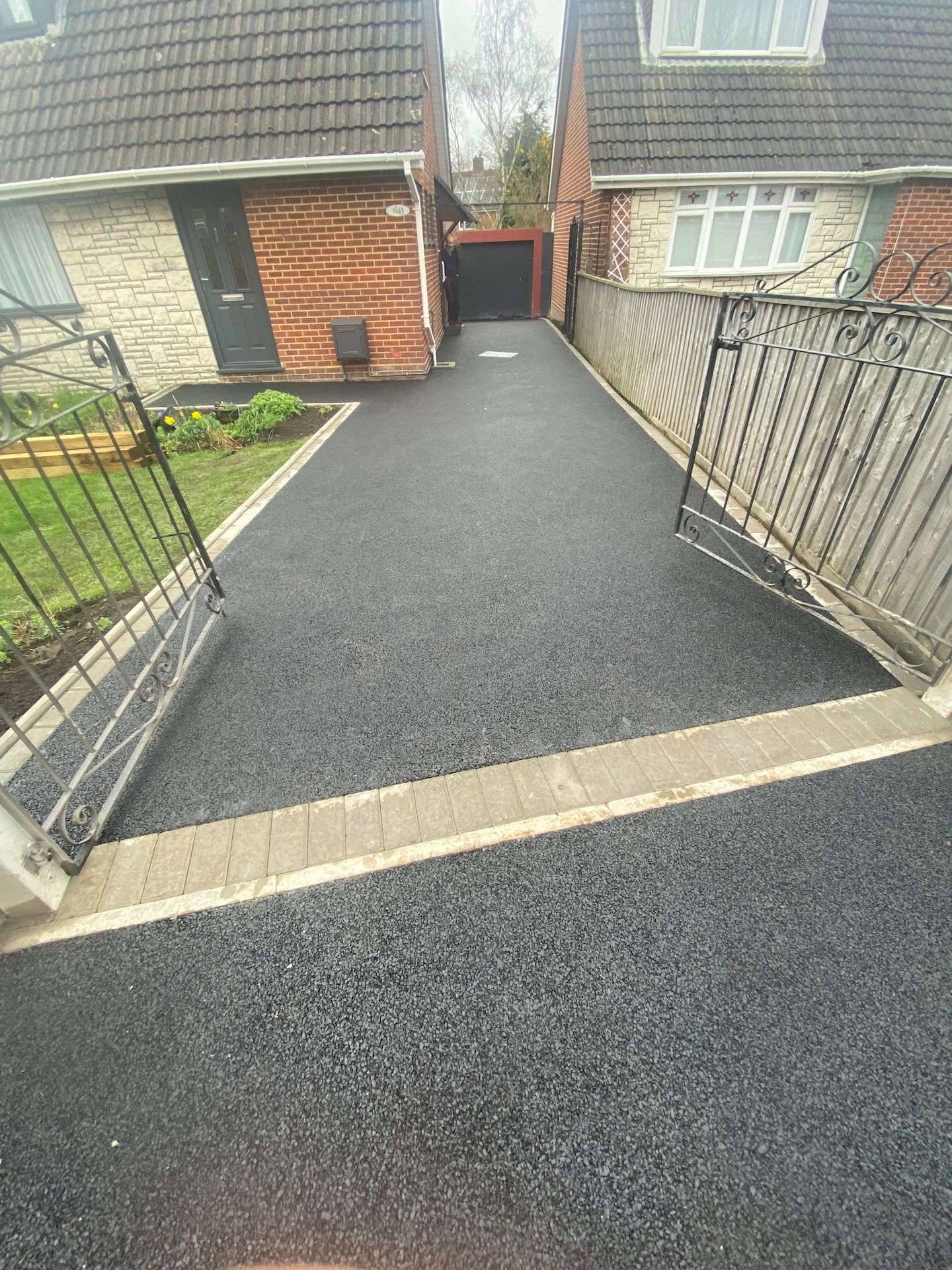 A black driveway leading to a house with a gate.