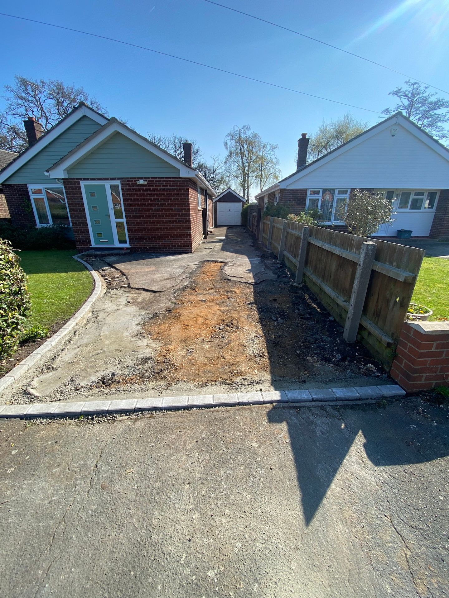 A dirt driveway leading to a brick house with a wooden fence.