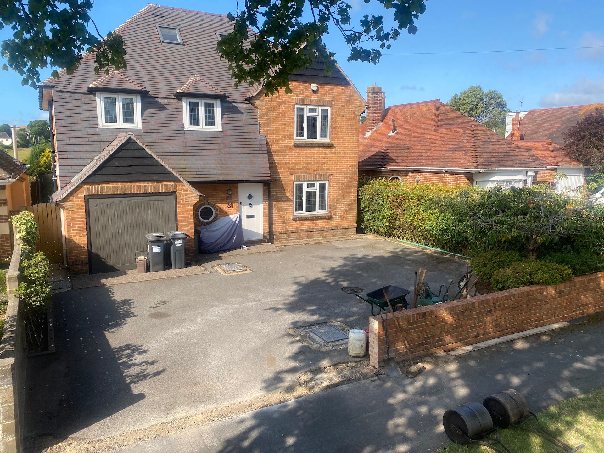 A large red brick house with a garage and a wheelbarrow in front of it.