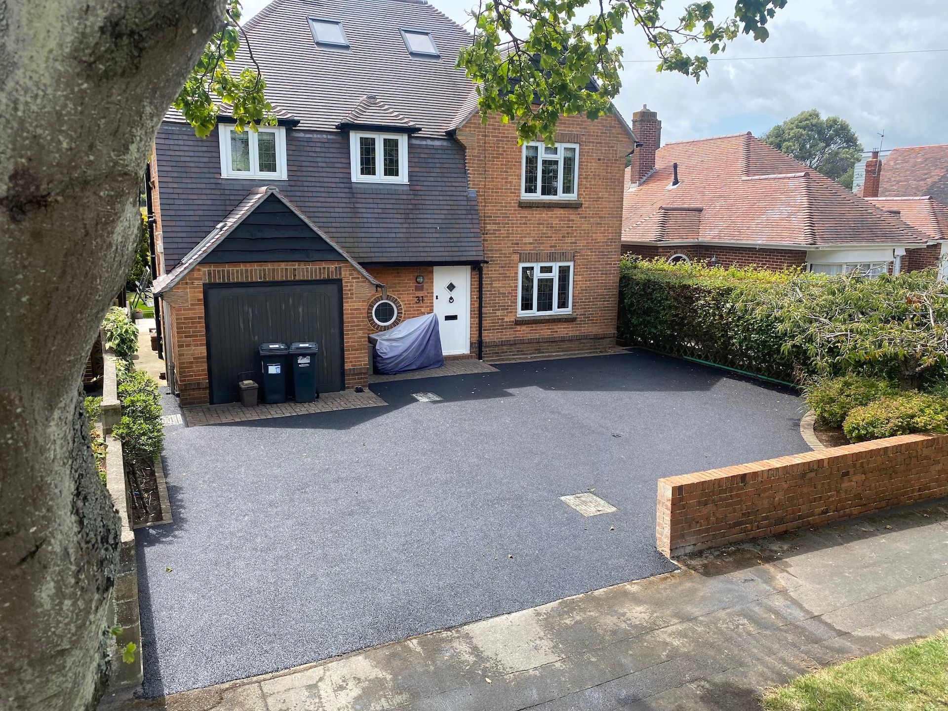 A large brick house with a black driveway and a tree in front of it.