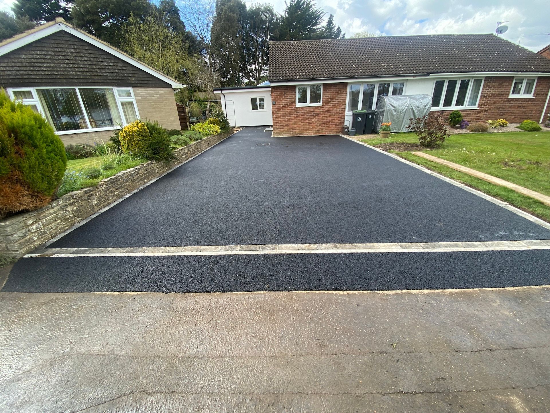 A brick house with a black driveway in front of it.