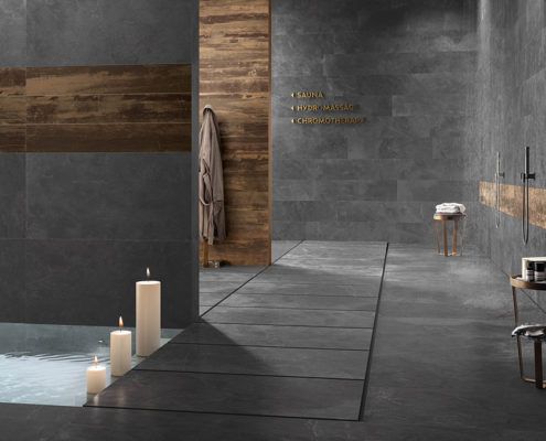 Ein Badezimmer mit dunkelgrauen Natursteinfliesen, einer Badewanne und Kerzen darin.