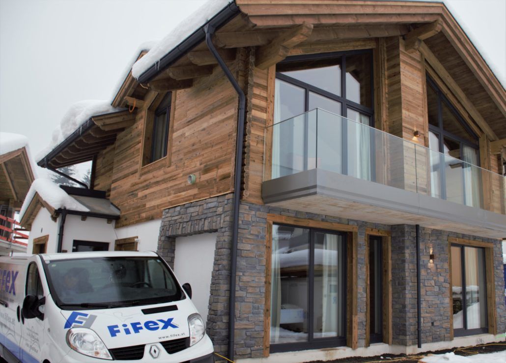Ein weißer Fifex-Van steht vor einem Haus mit Natursteinfassade.