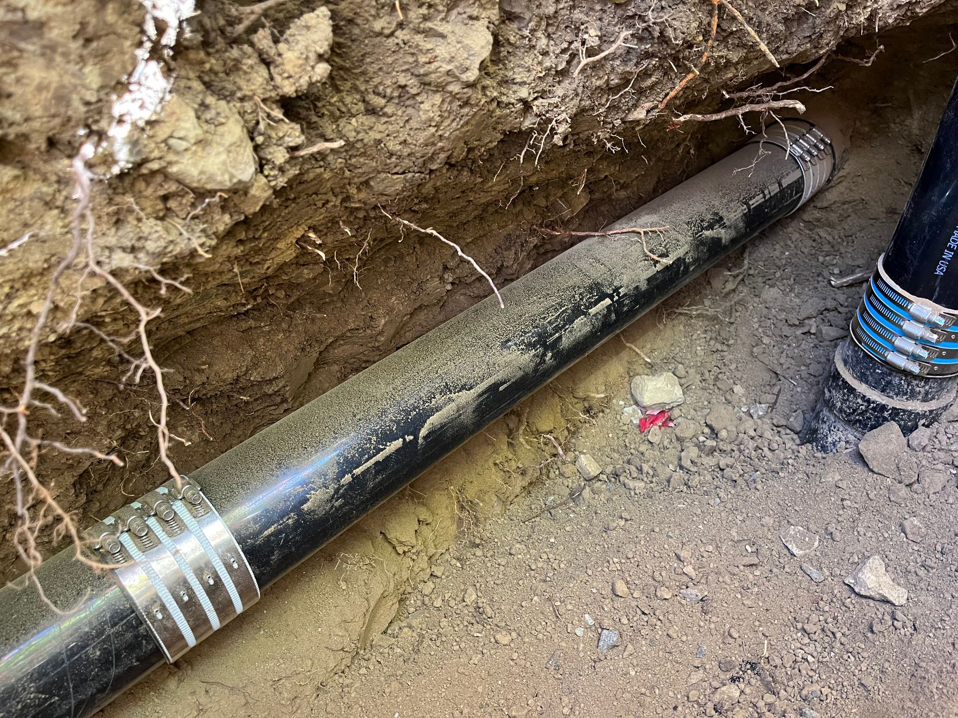 A black pipe is laying in the dirt in a trench.