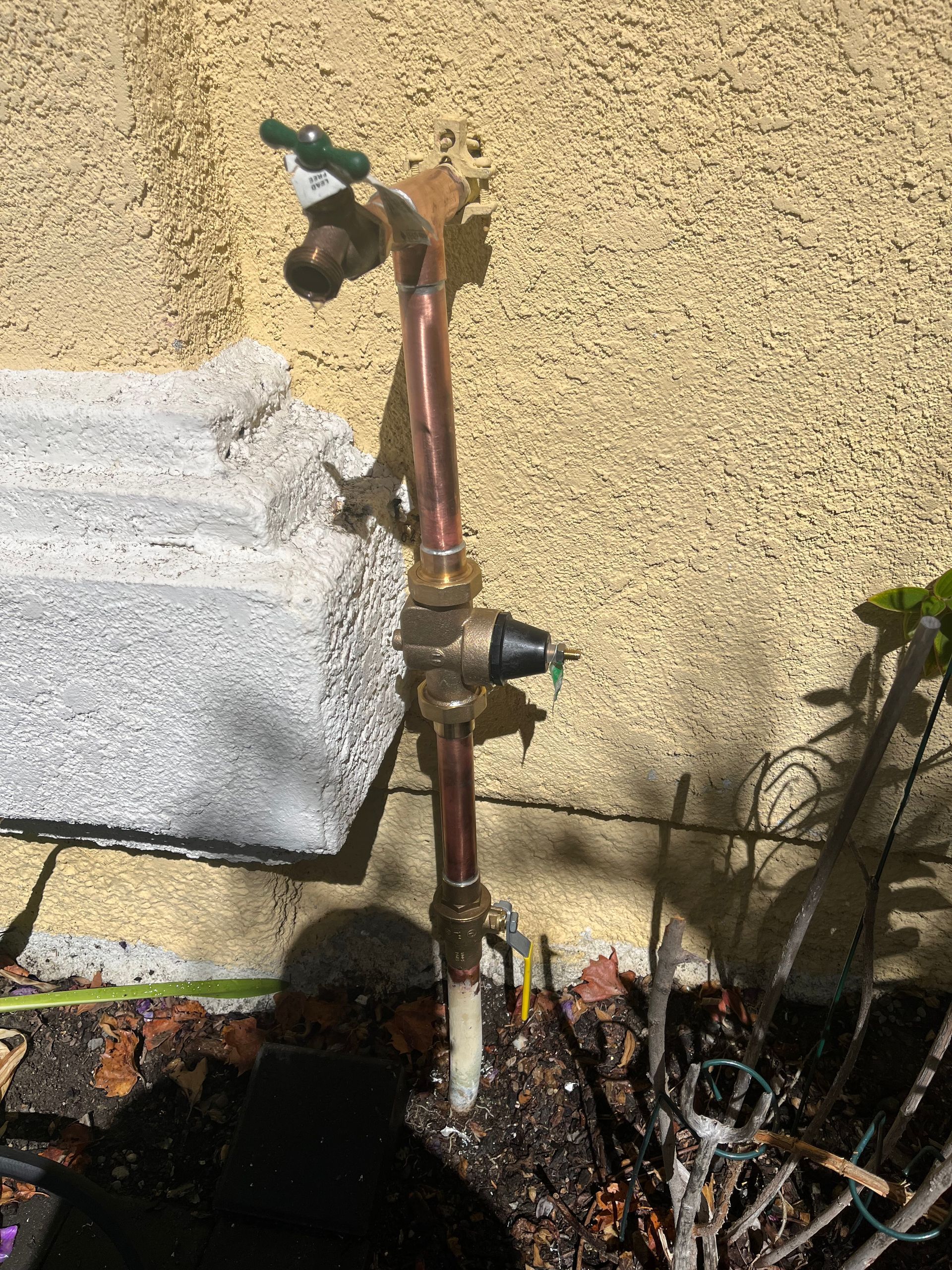 A copper pipe with a green handle is attached to a wall.