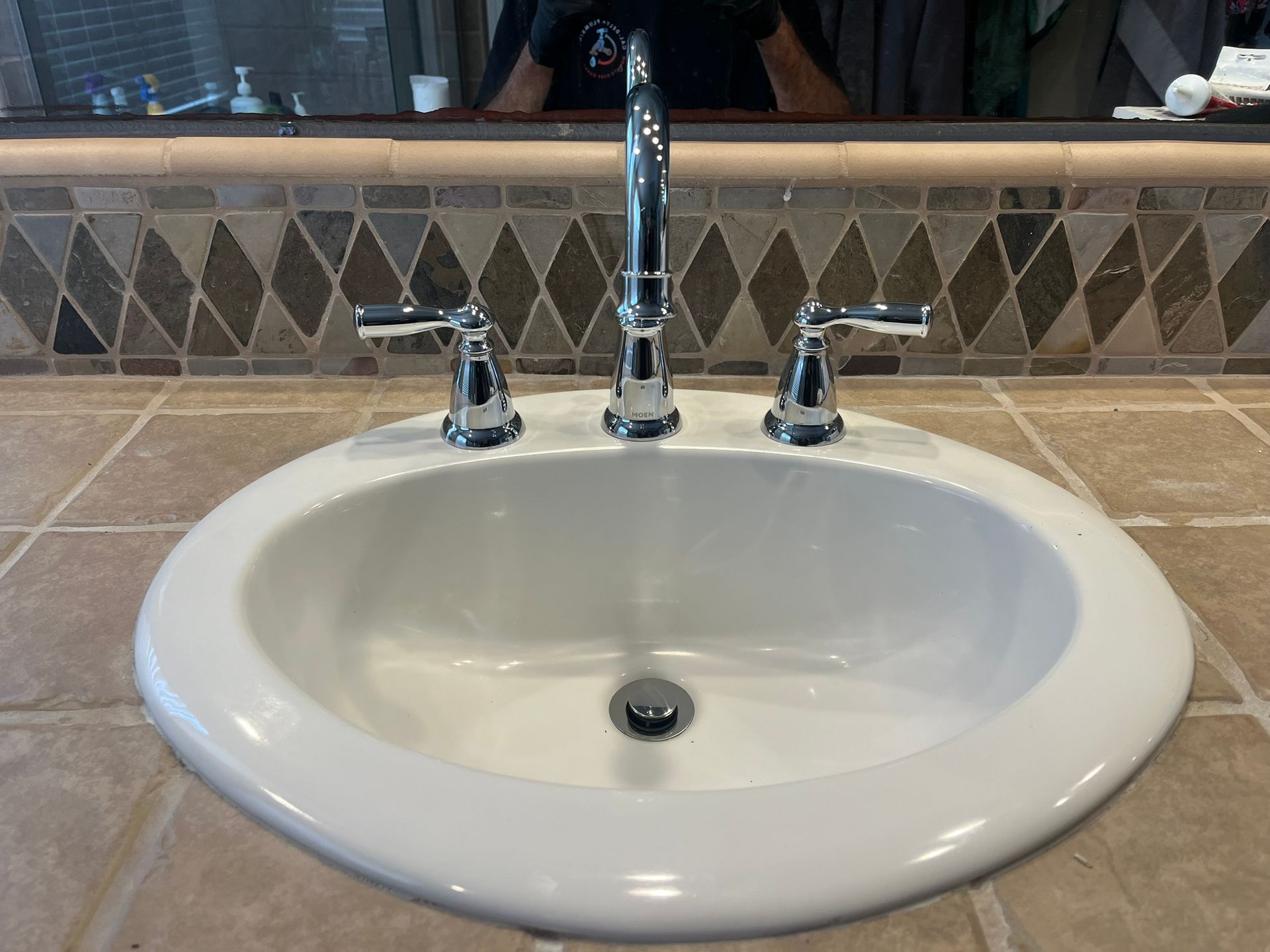 A bathroom sink with a man taking a picture of himself in the mirror