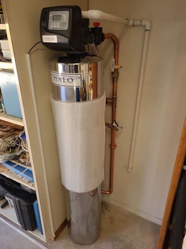 A water filter is sitting in a closet next to a copper pipe.