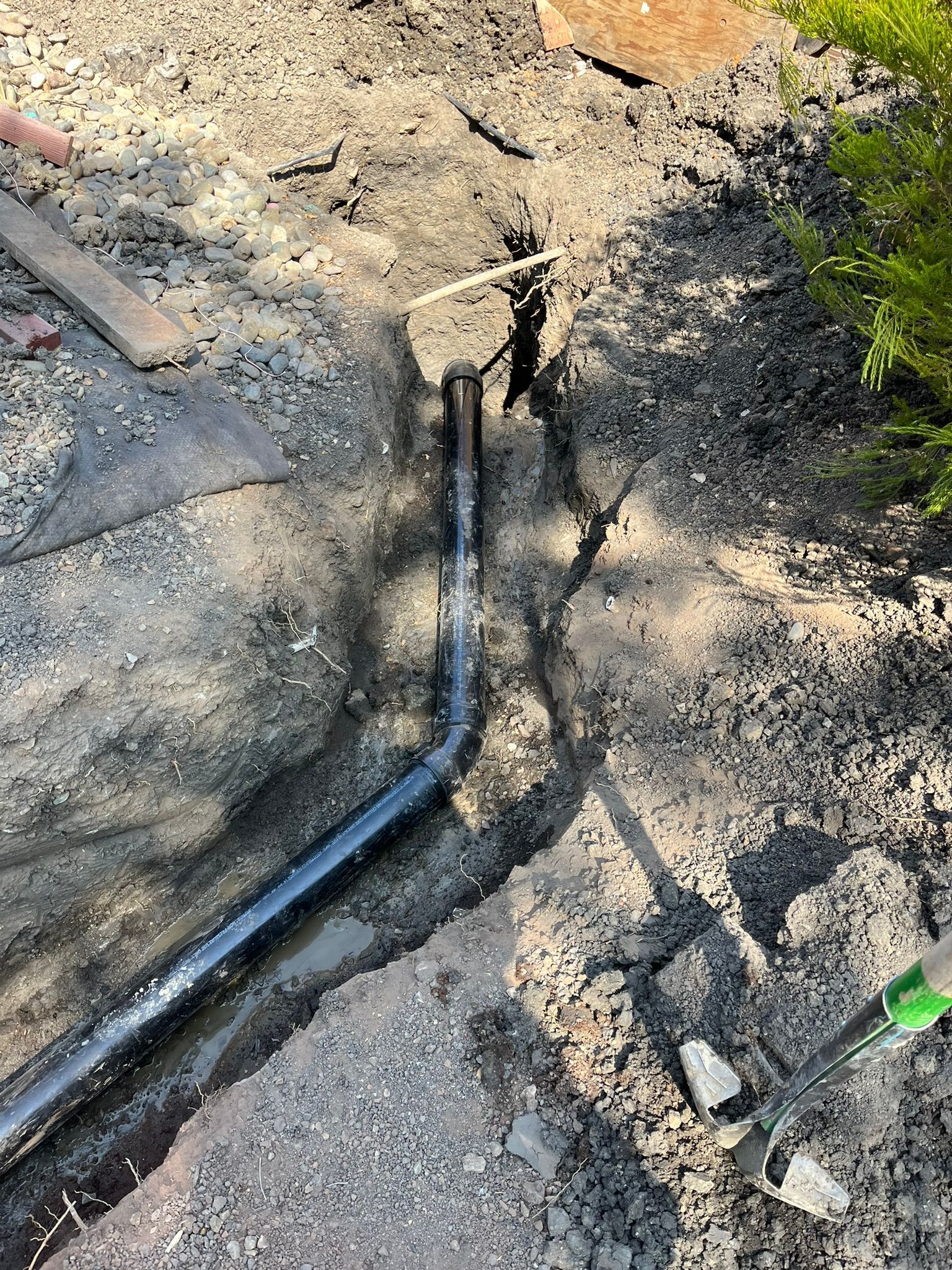 A pipe is laying in the dirt next to a rock.