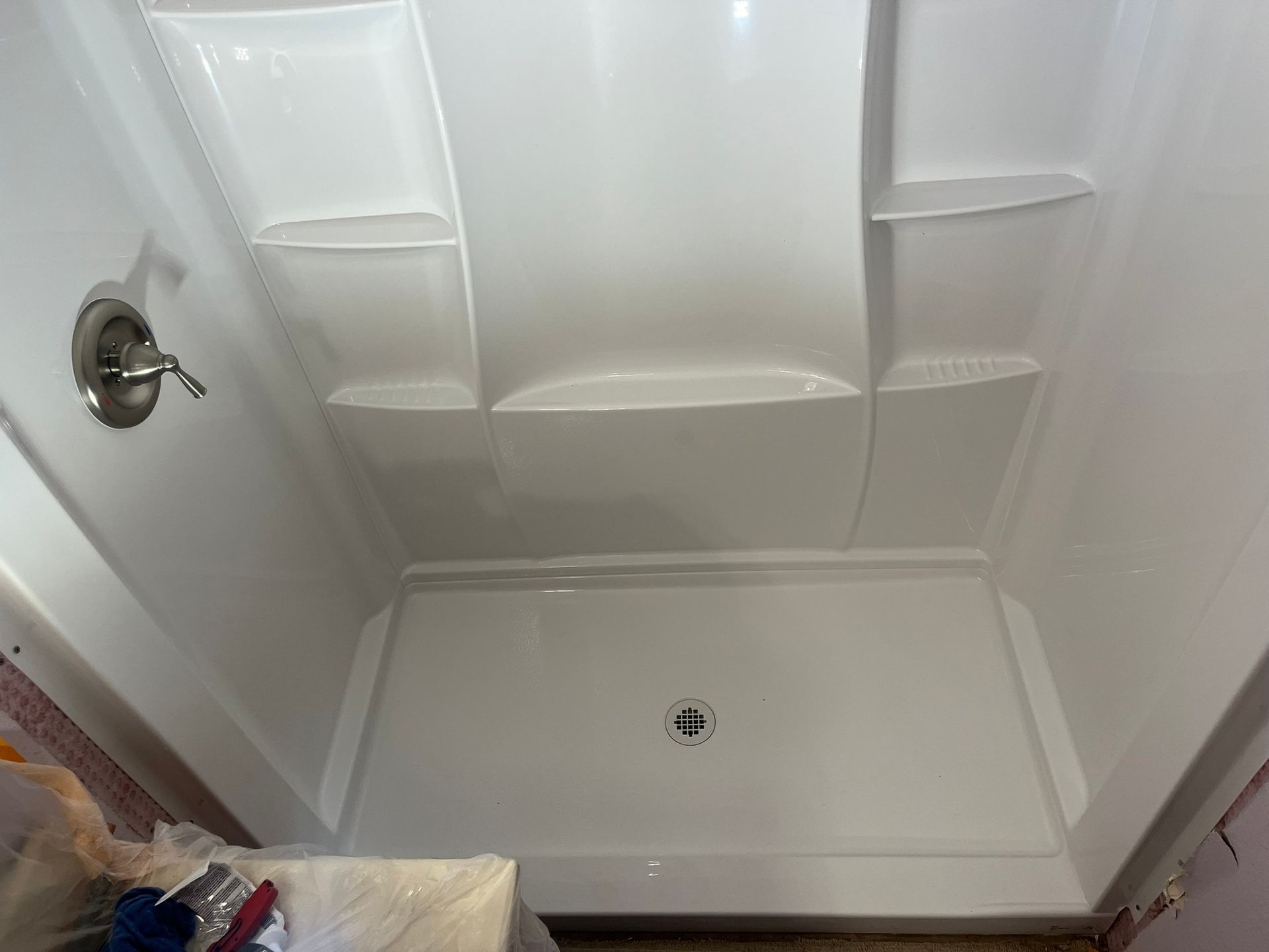 A white shower stall with shelves and a faucet in a bathroom.