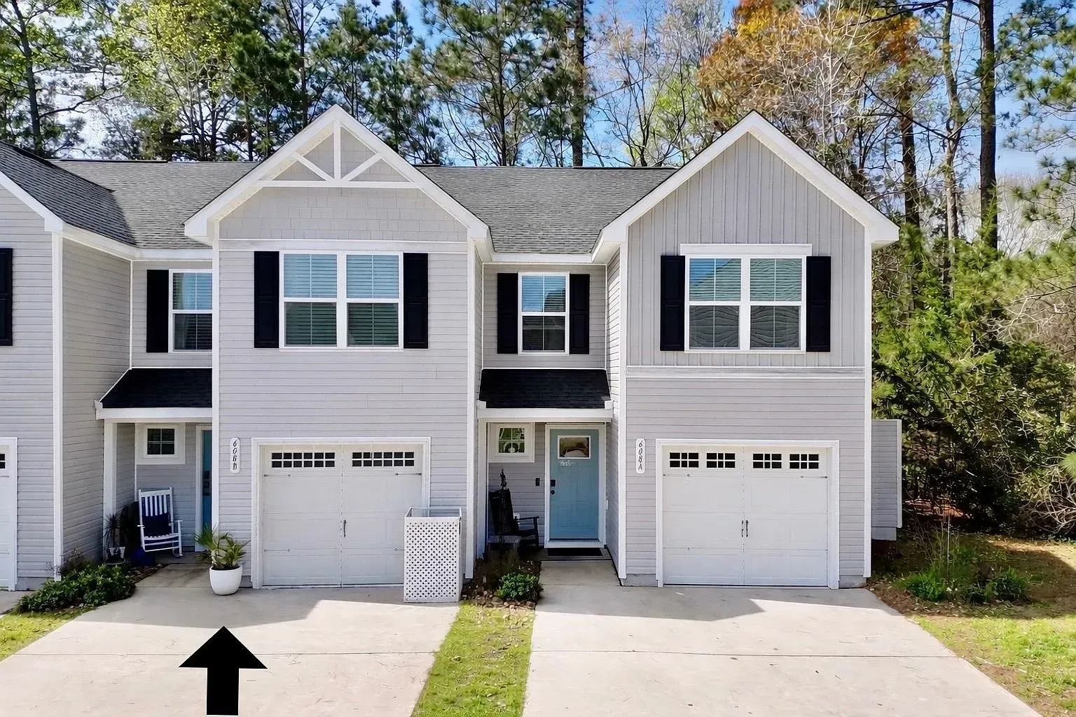 An exterior view of a two-story gray townhouse with a white garage door, featuring a black arrow pointing to the driveway.