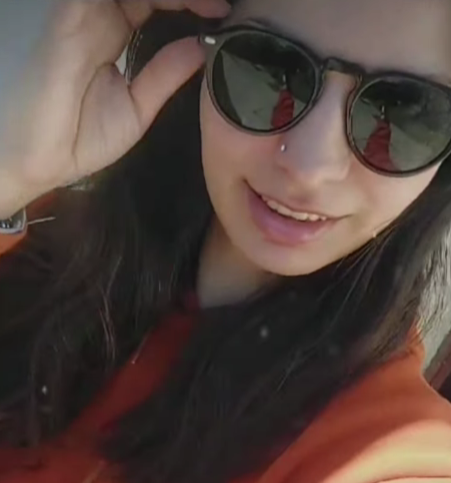 Mujer con gafas de sol se las ajusta sonriendo; al aire libre.