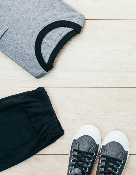 Camiseta gris con ribete negro, pantalones negros y zapatillas grises sobre una superficie de madera clara.