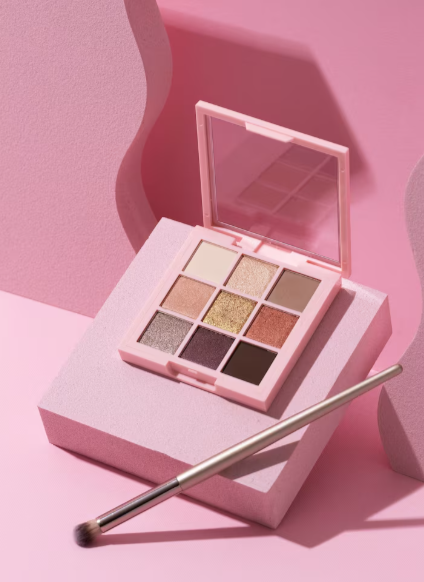 Paleta de sombras de ojos rosa con pincel sobre bloque rosa contra fondo ondulado rosa.
