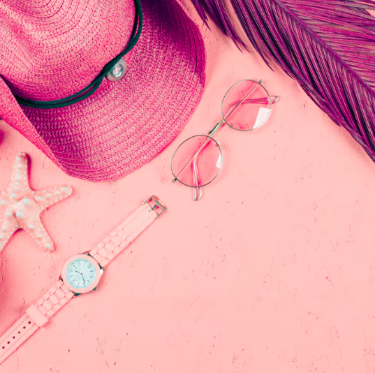 Sombrero de sol rosa, gafas de sol, reloj, estrella de mar y hoja sobre fondo rosa.