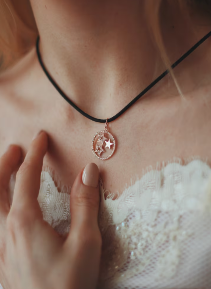 Persona que lleva un colgante de oro rosa con estrellas y luna en un collar negro tipo gargantilla.