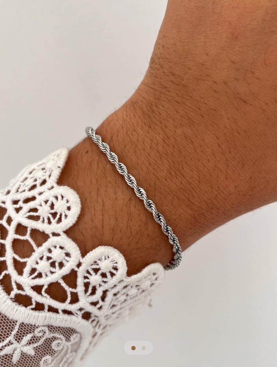 Pulsera de cuerda plateada en la muñeca, junto a una manga de encaje blanco.