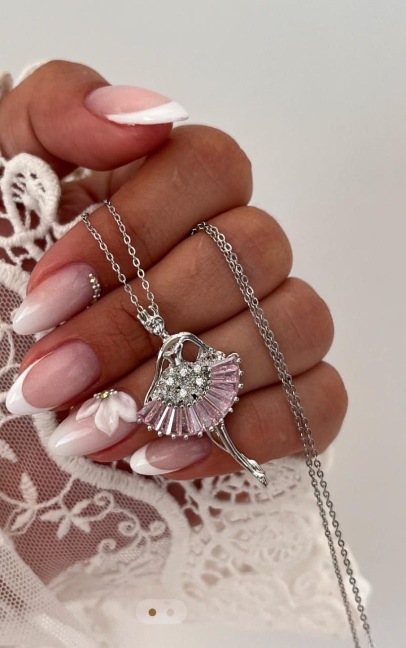 Mano sosteniendo un collar con colgante de bailarina de plata con tutú rosa y blanco.