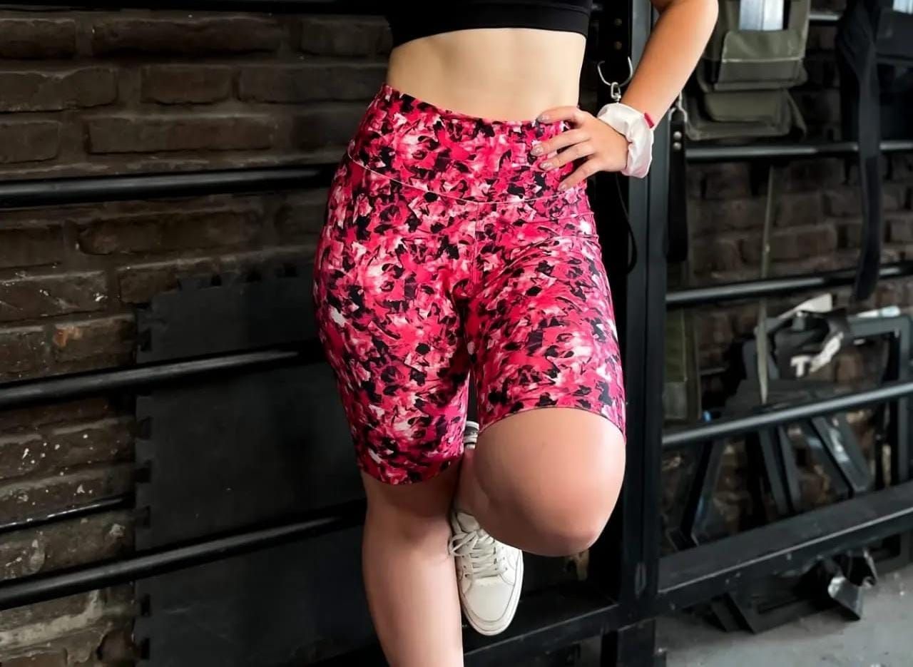 Mujer con pantalones cortos rosas estampados, apoyada contra una estructura de gimnasio