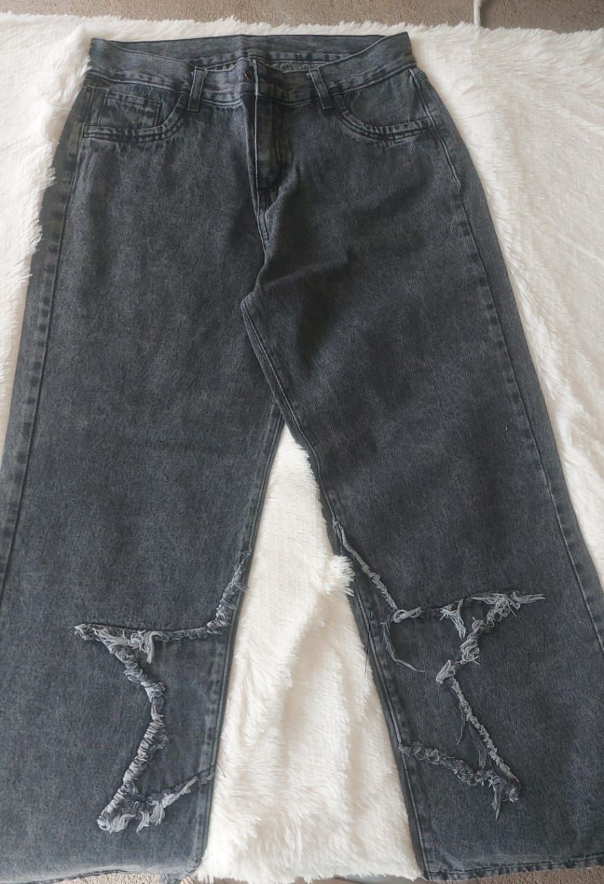 Pantalones vaqueros negros de mezclilla con aberturas desgastadas hasta la rodilla, sobre una superficie blanca y esponjosa.