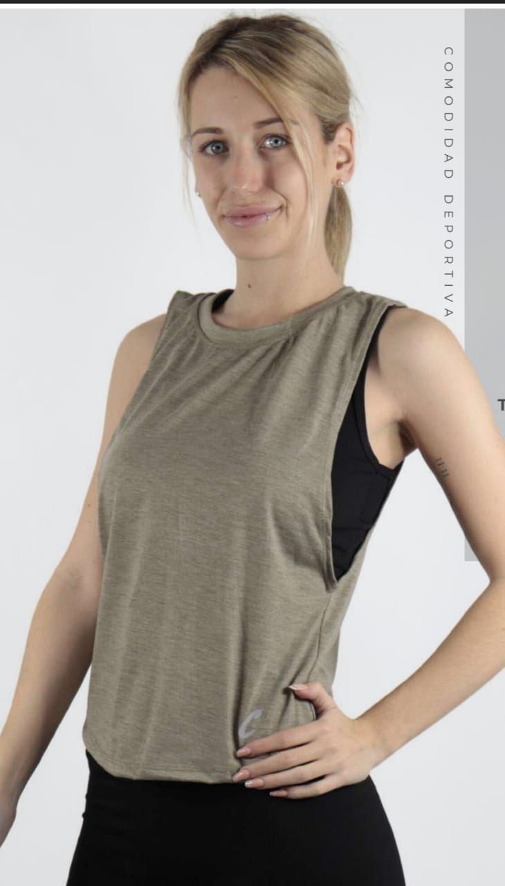 Mujer con camiseta de entrenamiento verde oliva y leggings negros, sonriendo con la mano en la cadera.