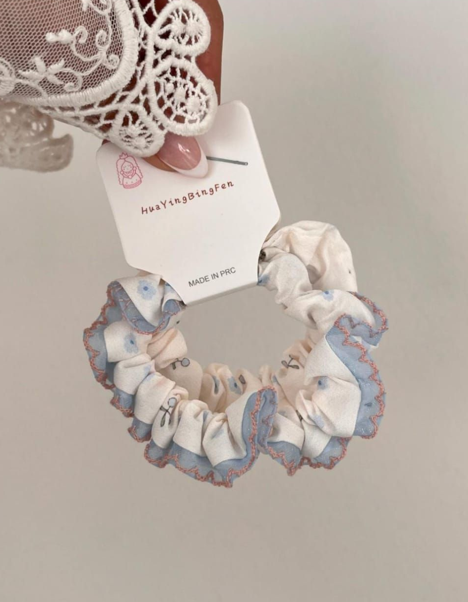 Coletero con estampado floral azul y ribete de volantes, sostenido por una mano.